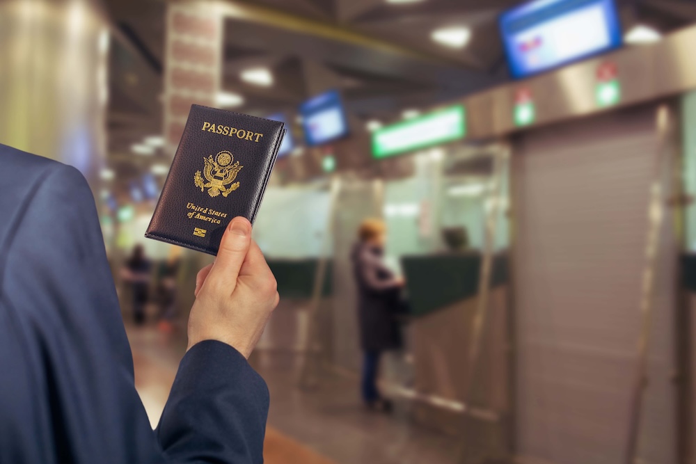 Man businessman in a blue suit with suitcase holding american passport with boarding pass in the airport opposite Immigration and passport control. concept. America. USA